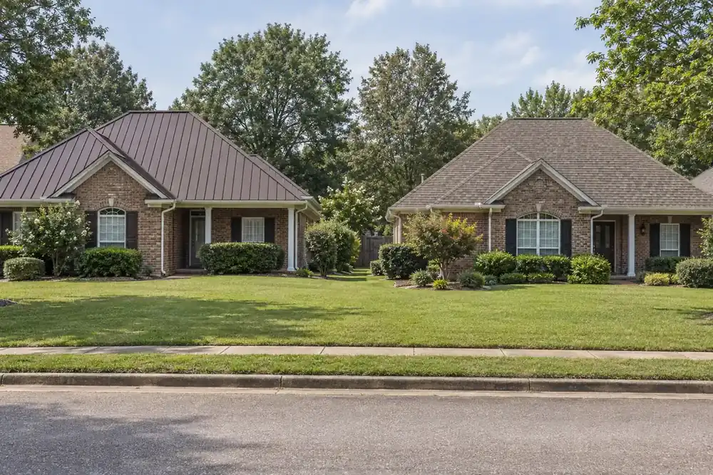 Neighboring brick houses with a bronze standing seam roof and a weathered wood shingle roof
