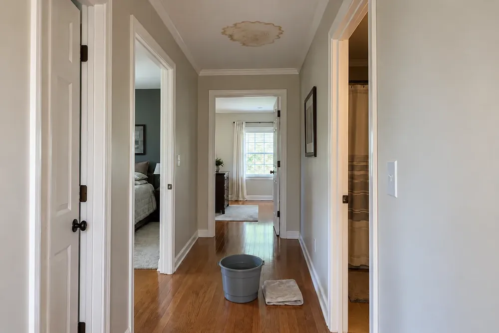 Brown water stain on a hallway ceiling with a bucket and towel on the wood floor below