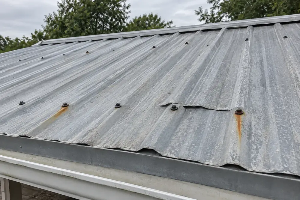 Rust streaks below exposed screws and a lifted lap on corrugated metal roofing