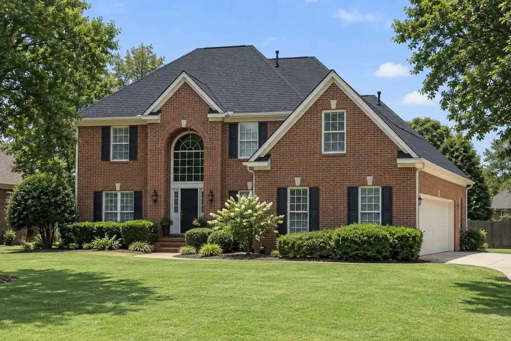 New dark-grey architectural shingle roof, black vent pipes and white trim on a two-story red-brick house