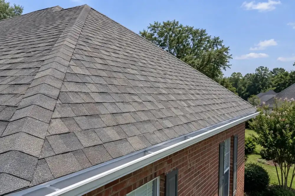 Hip roof with straight architectural shingle courses and ridge caps over a red brick home